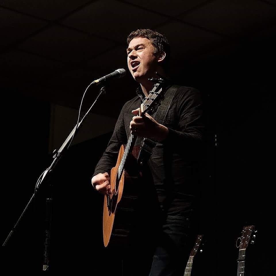 Tom holding a guitar and singing into a microphone