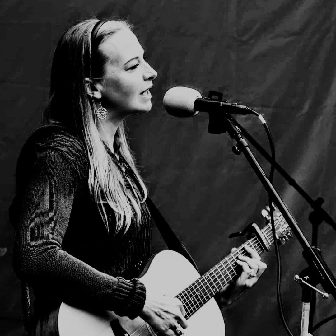 Sophie playing a guitar and singing into a microphone