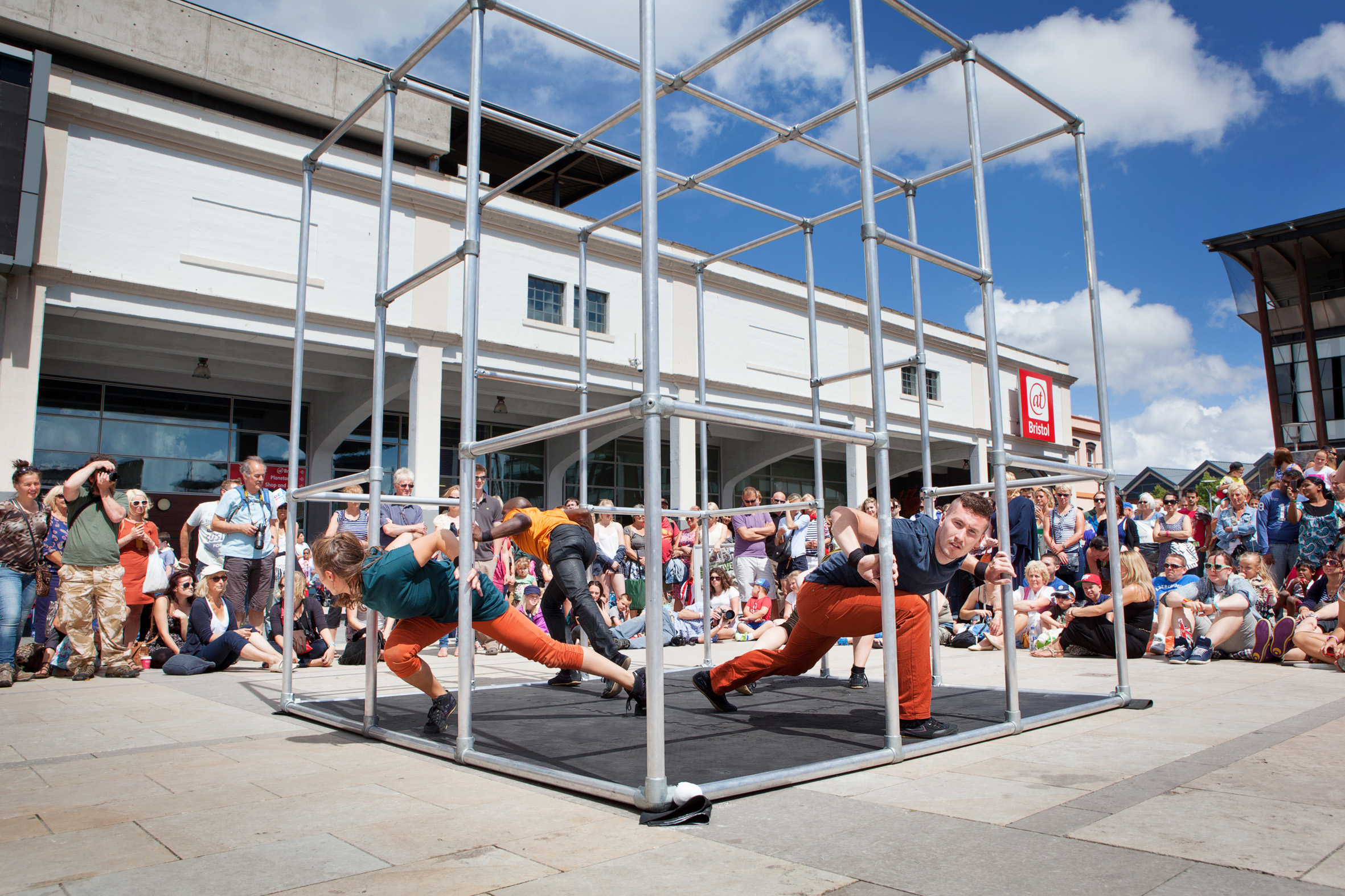 Motionhouse perform captive in a large cube cage outside @Bristol to a surrounding crowd
